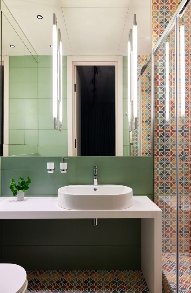This modern bathroom features green tiles, a sleek basin, and vibrant decor, creating an inviting atmosphere