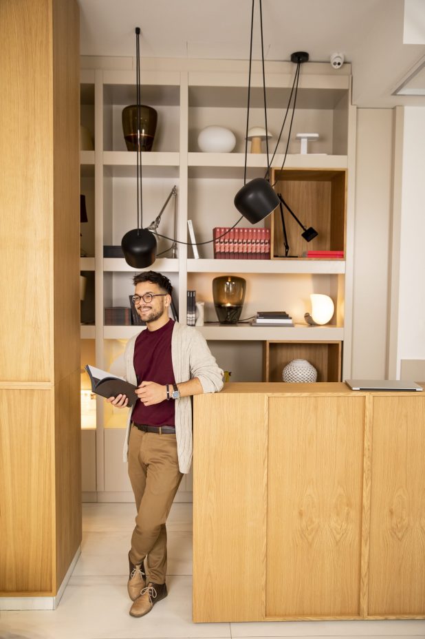 Handsome young man in casual clothes and with eyeglasses reading a book at home