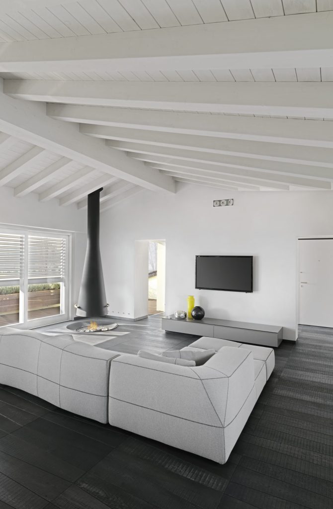 Interiors of  a modern living room with fireplace in the attic room, in the foreground the sofas, the floor and the ceiling are made of wood